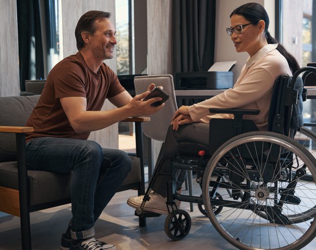 Jolly man with smartphone in office with female with disability